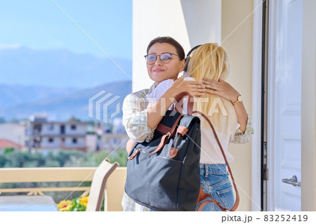 Mom hugging teenage daughter on the porch of the house near the front door, meeting goodbye. Mom hugging teenage daughter on the porch of the house near the front door, meeting goodbye. 83252419