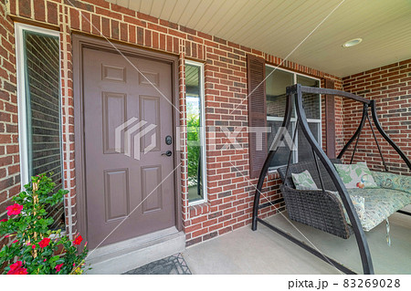 Home facade with brown front door between sidelights and swing bench on porch Home facade with brown front door between sidelights and swing bench on porch 83269028