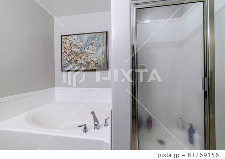 Built in bathtub and shower stall inside bathroom with floral painting on wall 83269156