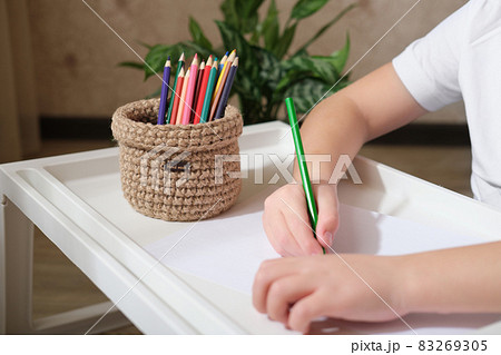 kid's hands drawing with color pencils and woven wicker basket for stationery storage. hand made basket for desktop order. crop view. kid's hands drawing with color pencils and woven wicker basket for stationery storage. hand made basket for desktop order. crop view. 83269305