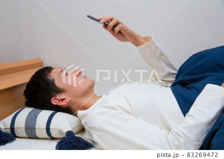 ベッドに横になりながらスマホを見ている若い日本人男性の写真素材