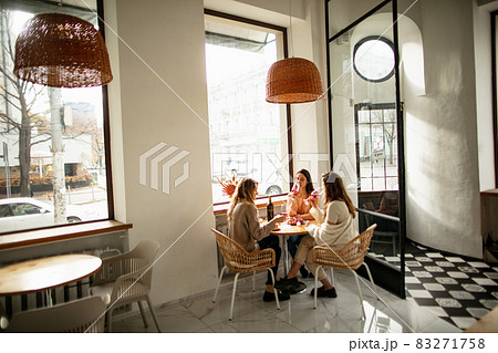Portrait of three beautiful women spending time together, having lunch with wine on warm sunny day 83271758