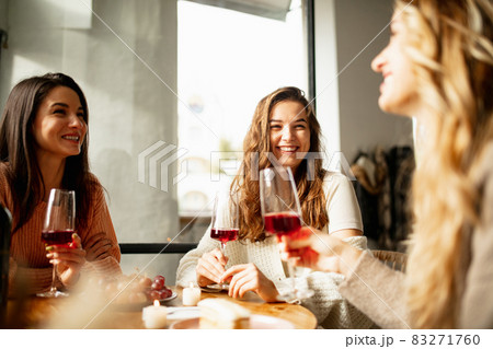 Portrait of three beautiful women sitting at cafe, talking and drinking red wine. Weekend gathering 83271760