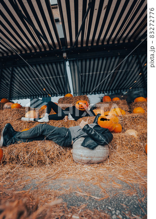 A guy and a girl with pumpkins on their heads are lying in the hay 83272776