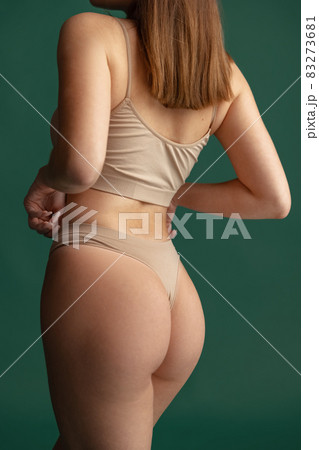 Cropped image of female body, back view in beige inner wear isolated over green background. Anti cellulite care 83273681