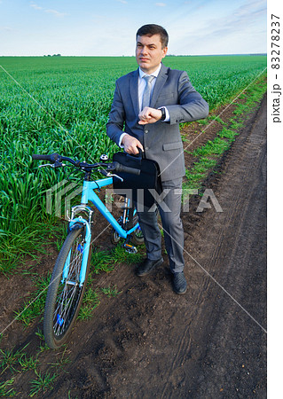Businessman with a bicycle looking at his wristwatch in a green grass field - business concept for freedom, vacation or freelance. Beautiful spring nature. 83278237
