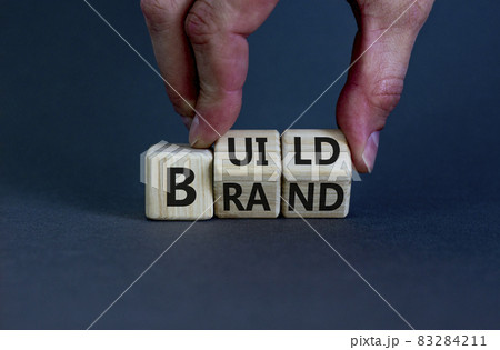 Build your brand symbol. Businessman turns wooden cubes and changes the word 'build' to 'brand'. Beautiful grey background. Build your brand and business concept. Copy space. Build your brand symbol. Businessman turns wooden cubes and changes the word 'build' to 'brand'. Beautiful grey background. Build your brand and business concept. Copy space. 83284211