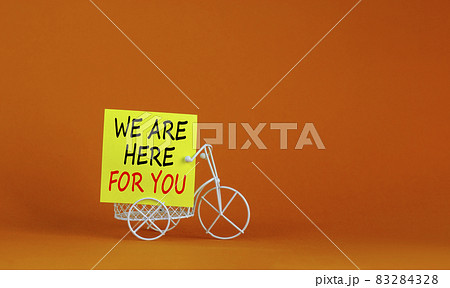 Help is here symbol. Wooden clothespin with yellow paper. Words 'we are here for you'. Miniature bicycle model. Beautiful orange background. Business and help is here support concept, copy space. 83284328