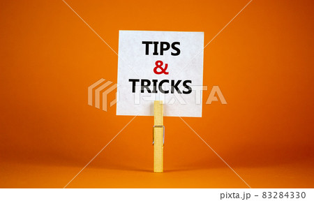 Tips and tricks symbol. White paper on wooden clothespin. Words 'Tips and tricks'. Beautiful orange background. Business and tips and tricks concept, copy space. Tips and tricks symbol. White paper on wooden clothespin. Words 'Tips and tricks'. Beautiful orange background. Business and tips and tricks concept, copy space. 83284330