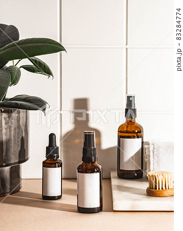 Amber bottles with white labels and houseplant in ceramic pot on beige table and wall white tiles. Amber bottles with white labels and houseplant in ceramic pot on beige table and wall white tiles. 83284774