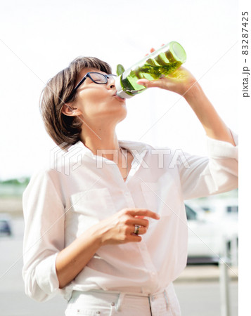 Thirsty woman drinks water from refilled green bottle. Useful transparent flask for liquids. Hot summer weather. Thirsty woman drinks water from refilled green bottle. Useful transparent flask for liquids. Hot summer weather. 83287425