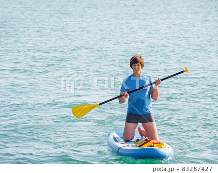 Handsome paddle boarder. Sportsman on knees paddling on stand up paddleboard. SUP surfing. Active lifestyle. Outdoor recreation. Vacation on seaside. 83287427