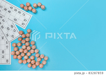 Wooden barrels with numbers and cards for playing lotto or bingo. Board game for the whole family. Blue background. Flat lay. Copy space. Place for advertising text. Wooden barrels with numbers and cards for playing lotto or bingo. Board game for the whole family. Blue background. Flat lay. Copy space. Place for advertising text. 83287859