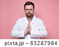 Serious, confident doctor in a white coat folded hands in supplication, palms together and calmly 83287984