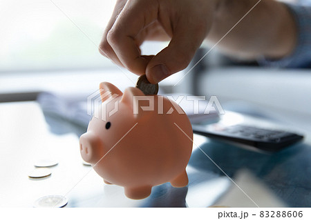 Crop close up man putting coin into pink piggy bank Crop close up man putting coin into pink piggy bank 83288606