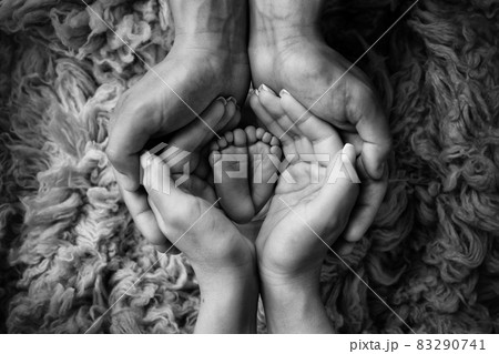 Legs and toes of a newborn. Parents hold the legs of the newborn in their palms. The palms of the father and mother. Black and white photo. Legs and toes of a newborn. Parents hold the legs of the newborn in their palms. The palms of the father and mother. Black and white photo. 83290741