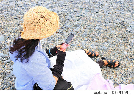 旅先の海辺で携帯を操作する女性の姿 83291699
