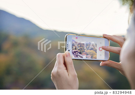 夕方、紅葉をスマホで撮影をする若い女性手元 83294948