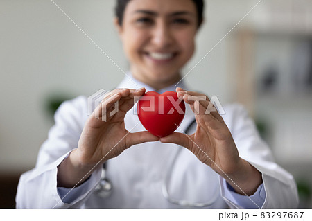 Smiling female cardiologist holding red heart, showing object at camera 83297687