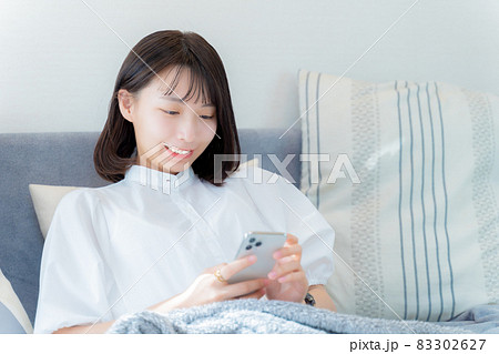 ソファに座ってスマホを見る笑顔の女性 ソファに座ってスマホを見る笑顔の女性 83302627