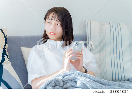 スマホを持ちながら外を眺める女性 83304334