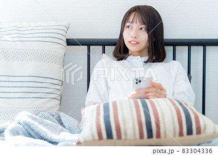 クッションを膝に乗せて座る女性 83304336