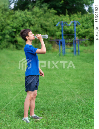 teenage boy exercising outdoors, sports ground in the yard, he opens a bottle of water and drinks, healthy lifestyle teenage boy exercising outdoors, sports ground in the yard, he opens a bottle of water and drinks, healthy lifestyle 83305924