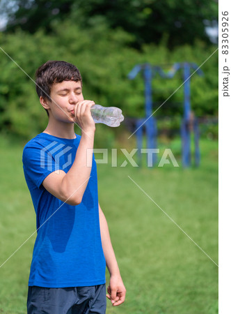 teenage boy exercising outdoors, sports ground in the yard, he opens a bottle of water and drinks, healthy lifestyle 83305926