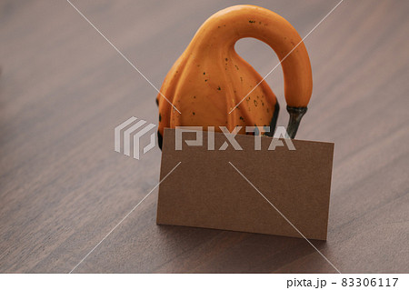 Small two tone decorative pear shaped pumpkin on black walnut table with empty paper card 83306117