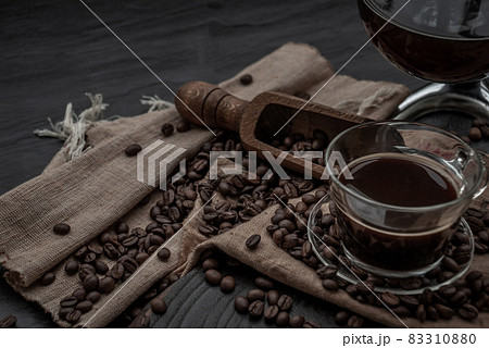 Cup of coffee and coffee beans roating with old wooden scoop and coffee beans around on the wooden and dark stone background. Oblique view from the top with copy space for your text. Cup of coffee and coffee beans roating with old wooden scoop and coffee beans around on the wooden and dark stone background. Oblique view from the top with copy space for your text. 83310880