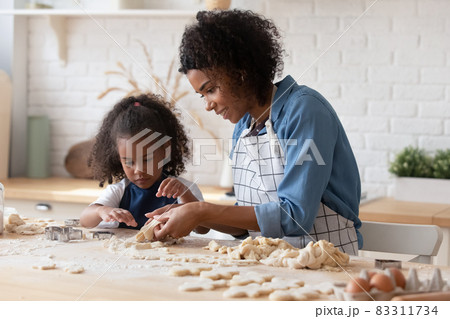 Smiling African American mother with little daughter cooking cookies Smiling African American mother with little daughter cooking cookies 83311734