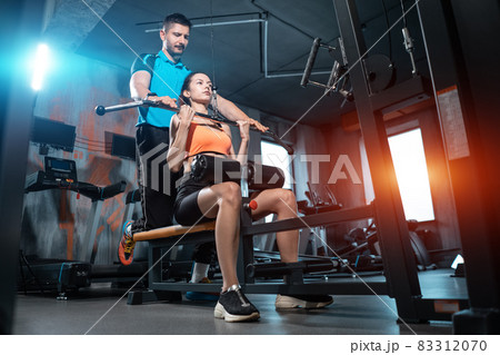 young fitness sporty female exercising pulldown with personal trainer in gym young fitness sporty female exercising pulldown with personal trainer in gym 83312070