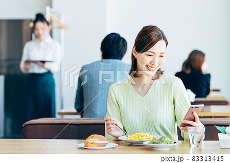 カフェで食事しながらスマホを見る若い女性 カフェで食事しながらスマホを見る若い女性 83313415