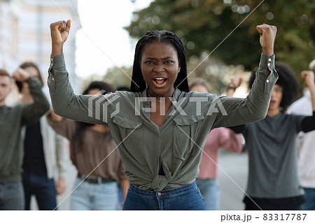 Black lady guiding multiracial group of activists, rasising fists up 83317787