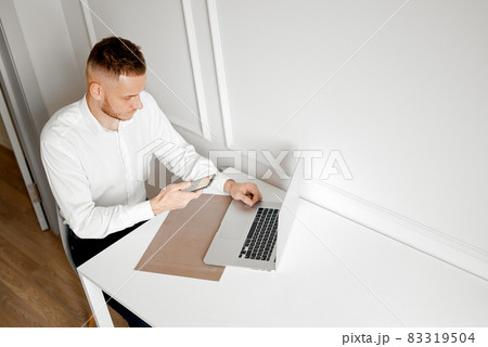 A young man works at home in a phone next to a laptop A young man works at home in a phone next to a laptop 83319504