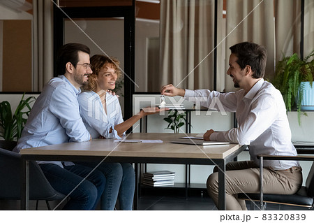 Realtor giving key from first home to happy family couple Realtor giving key from first home to happy family couple 83320839