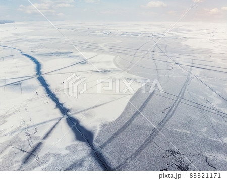 Aerial drone top view of snow covered frozen lake or river surface with big cracked ice diagonal lines. Natural winter landscape abstract texture pattern. Dangerous pond melting at thaw season 83321171