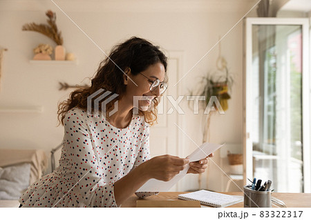 Happy Latin woman wearing glasses, reading paper letter 83322317