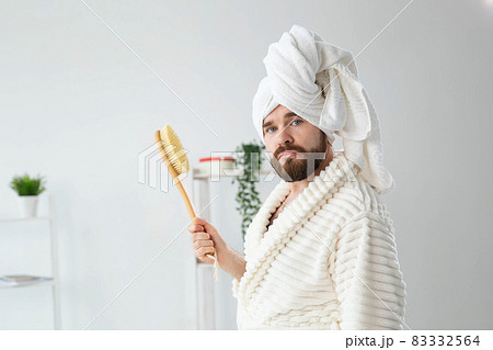 Portrait of funny guy wear turban towel holding in hands massage brush while sits on sofa. Male skin care and spa concept. Portrait of funny guy wear turban towel holding in hands massage brush while sits on sofa. Male skin care and spa concept. 83332564