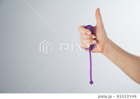 A woman recommends an electronic Kegel trainer for training pelvic floor muscles on a white background. Thumb up 83333549