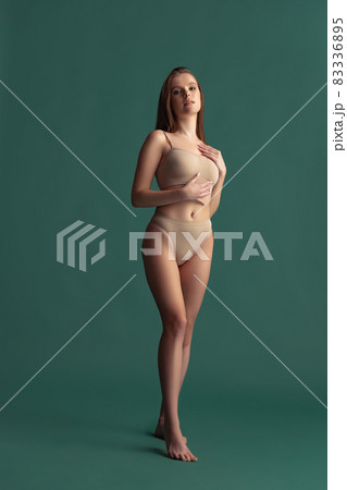 Full-length portrait of beautiful tender woman posing in beige underwear isolated over green background Full-length portrait of beautiful tender woman posing in beige underwear isolated over green background 83336895