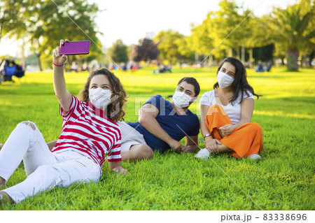 Three friends sitting on the grass and taking a selfie Three friends sitting on the grass and taking a selfie 83338696