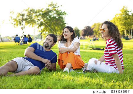 Three friends sitting on the grass in the park 83338697