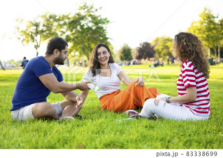Three friends sitting on the grass in the park Three friends sitting on the grass in the park 83338699