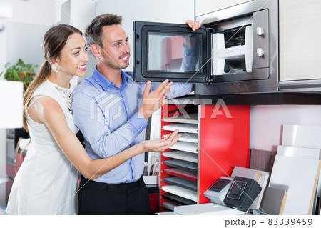 Happy young couple looking new microwave Happy young couple looking new microwave 83339459