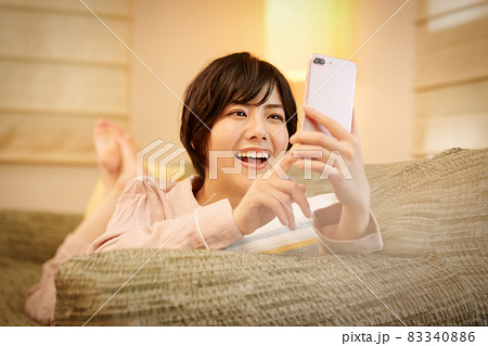 ソファに寝転んでスマホを見る若い女性 ソファに寝転んでスマホを見る若い女性 83340886