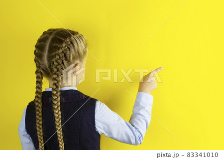 Schoolgirl stands with her back pointing her finger at free empty space for text or advertising, standing isolated on yellow studio background Schoolgirl stands with her back pointing her finger at free empty space for text or advertising, standing isolated on yellow studio background 83341010