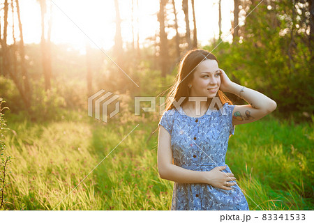 Beautiful girl in a blue summer dress in the rays of the sunset in the park. 83341533