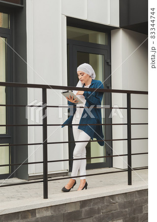 Smiling muslim girl using digital tablet, browsing Internet or social networks outdoor 83344744