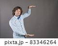 Horizontal shot of handsome Caucasian man with bristle, shows height of something with both hands, pretends holding item or thing, demonstrates size, wearing shirt and bow-tie, isolated on grey 83346264